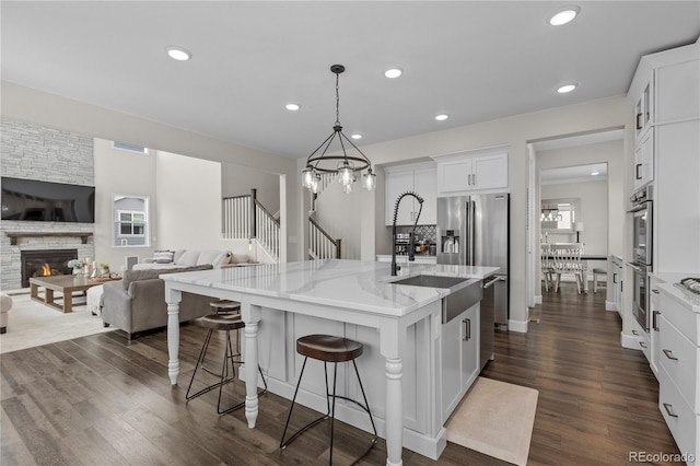 kitchen featuring pendant lighting, white cabinetry, an island with sink, light stone counters, and a breakfast bar area