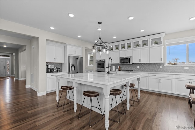 kitchen with decorative light fixtures, white cabinets, appliances with stainless steel finishes, and a center island with sink