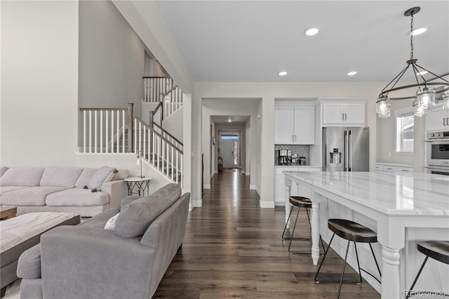 kitchen with light stone countertops, white cabinets, appliances with stainless steel finishes, decorative light fixtures, and decorative backsplash