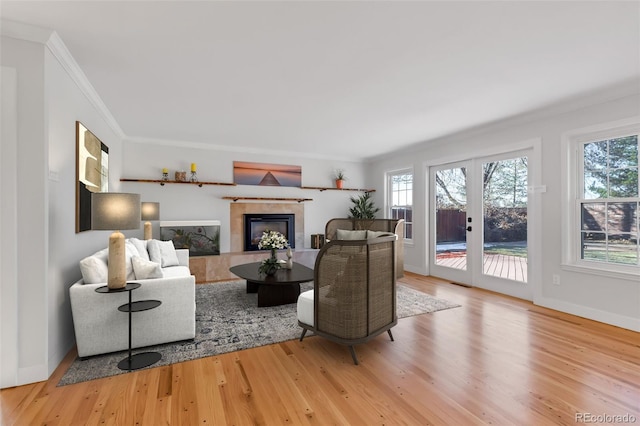 living room with a fireplace, crown molding, light hardwood / wood-style flooring, and french doors