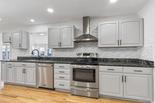 kitchen featuring sink, wall chimney exhaust hood, light hardwood / wood-style flooring, decorative backsplash, and appliances with stainless steel finishes