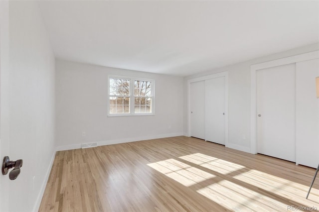 unfurnished bedroom with light hardwood / wood-style floors and two closets