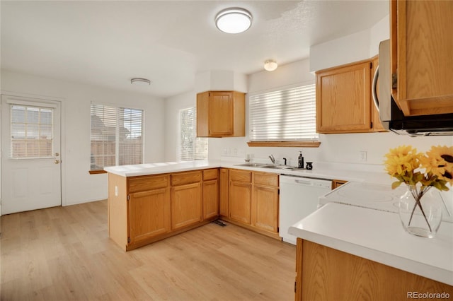 kitchen featuring light countertops, light wood-style floors, white dishwasher, a sink, and a peninsula