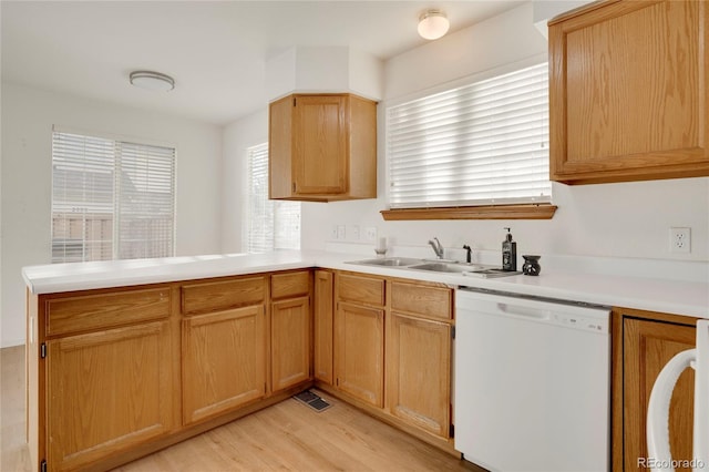 kitchen with light countertops, light wood-style floors, white dishwasher, a sink, and a peninsula