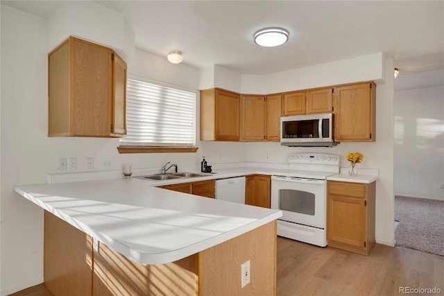 kitchen featuring a breakfast bar area, a peninsula, white appliances, a sink, and light countertops