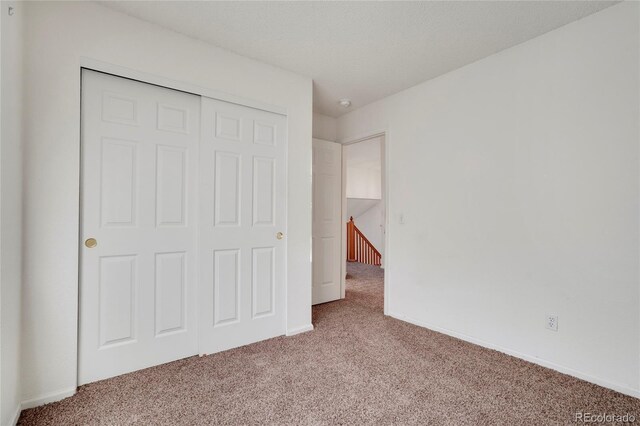 unfurnished bedroom featuring carpet floors, a textured ceiling, baseboards, and a closet