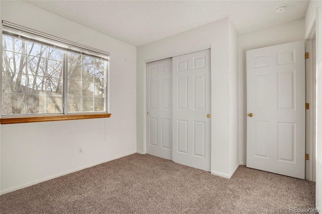 unfurnished bedroom featuring a textured ceiling, a closet, baseboards, and light colored carpet