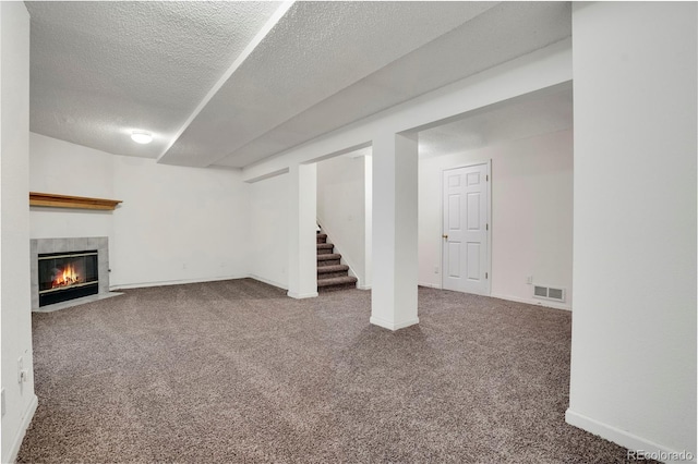 finished basement featuring visible vents, stairway, carpet flooring, a textured ceiling, and a tile fireplace