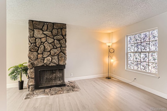 living room with a stone fireplace, wood-type flooring, and a textured ceiling