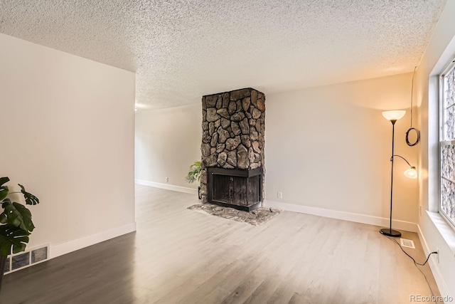 living room featuring a stone fireplace, hardwood / wood-style floors, a healthy amount of sunlight, and a textured ceiling