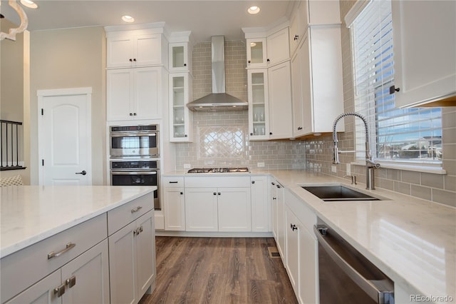 kitchen with tasteful backsplash, wall chimney exhaust hood, dark wood-style flooring, stainless steel appliances, and a sink