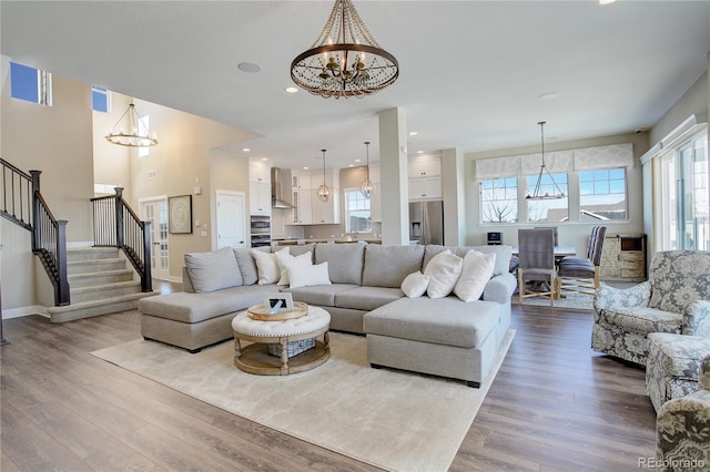 living area featuring dark wood-style floors, plenty of natural light, stairway, and a notable chandelier