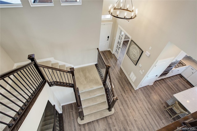 stairs featuring a notable chandelier, wood finished floors, a towering ceiling, and baseboards