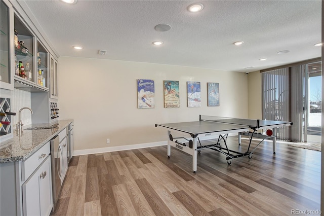 recreation room with a textured ceiling, baseboards, a sink, and wood finished floors