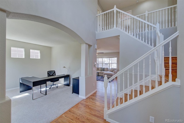 office space with wood finished floors, arched walkways, carpet floors, baseboards, and a high ceiling