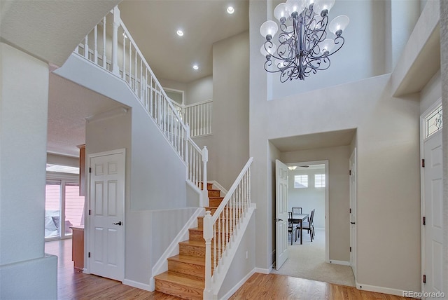 interior space with a towering ceiling, recessed lighting, a notable chandelier, wood finished floors, and stairs