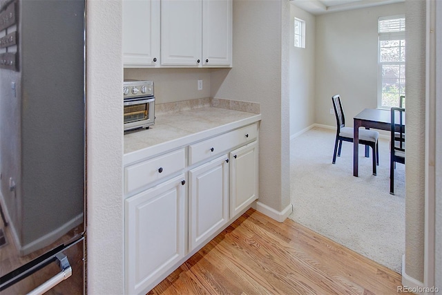 kitchen featuring light countertops, fridge, baseboards, and white cabinetry