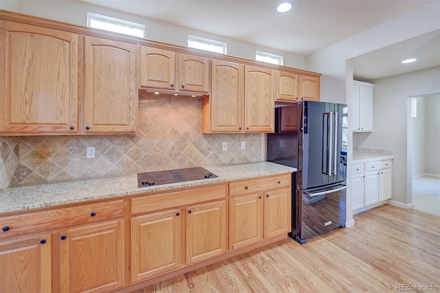 kitchen with black appliances, a wealth of natural light, light stone countertops, and light wood-style floors