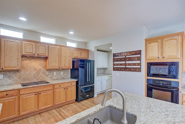 kitchen featuring light stone counters, a sink, light wood-style flooring, black appliances, and tasteful backsplash