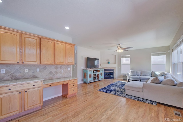 living area with light wood-style flooring, baseboards, visible vents, built in desk, and ceiling fan