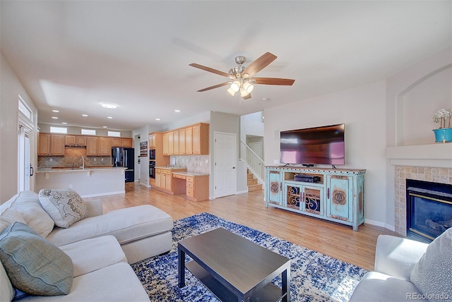 living room featuring light wood-type flooring, ceiling fan, a tiled fireplace, baseboards, and recessed lighting