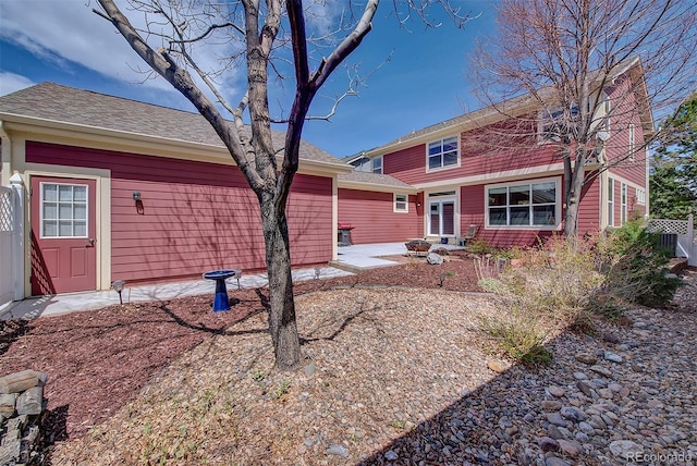 back of property with fence, a patio, and a shingled roof