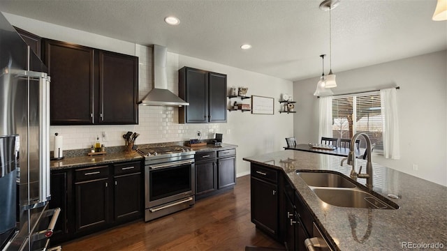 kitchen featuring dark hardwood / wood-style flooring, dark stone counters, stainless steel appliances, sink, and wall chimney range hood