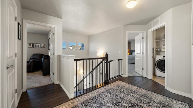 hallway featuring a textured ceiling, washer / clothes dryer, and dark wood-type flooring