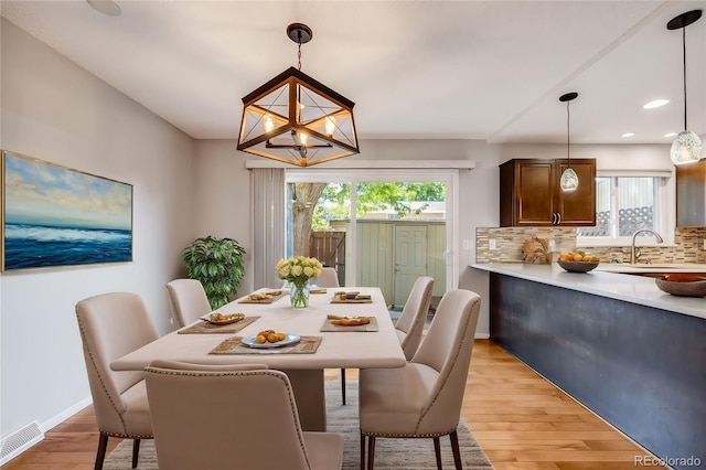 dining space featuring sink, light wood-type flooring, and an inviting chandelier