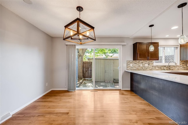 unfurnished dining area featuring light hardwood / wood-style floors, sink, a textured ceiling, and a notable chandelier