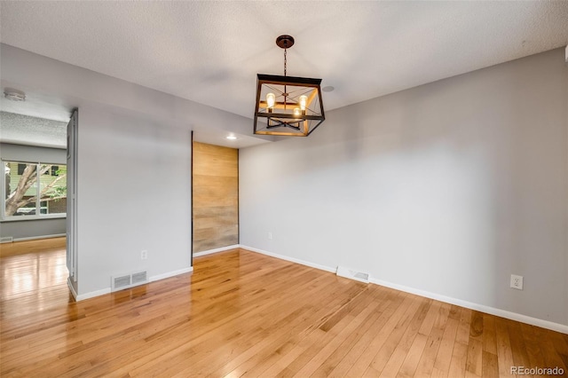 empty room featuring hardwood / wood-style floors, a textured ceiling, and a notable chandelier