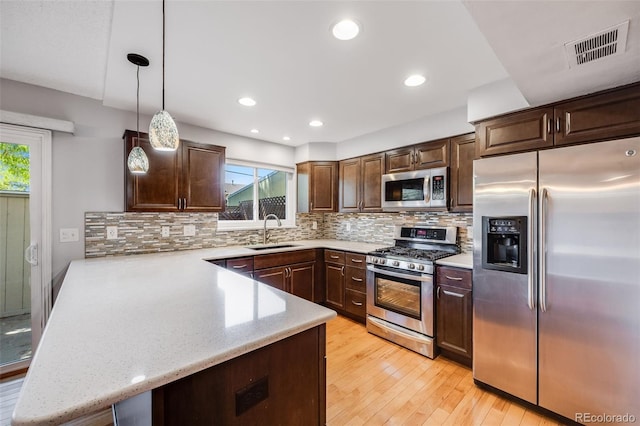 kitchen featuring kitchen peninsula, hanging light fixtures, appliances with stainless steel finishes, sink, and dark brown cabinetry