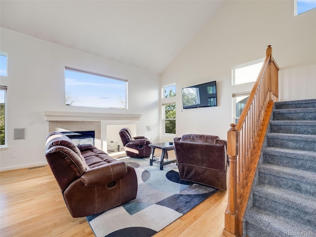 living area featuring high vaulted ceiling, stairway, wood finished floors, a tiled fireplace, and baseboards