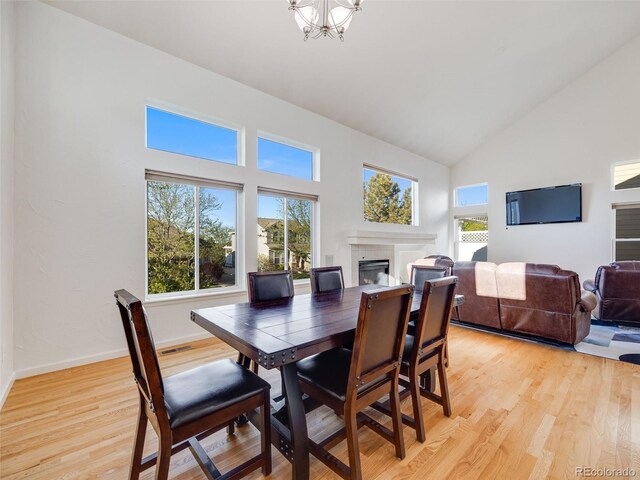 dining space featuring high vaulted ceiling, a tile fireplace, light wood-style floors, a chandelier, and baseboards