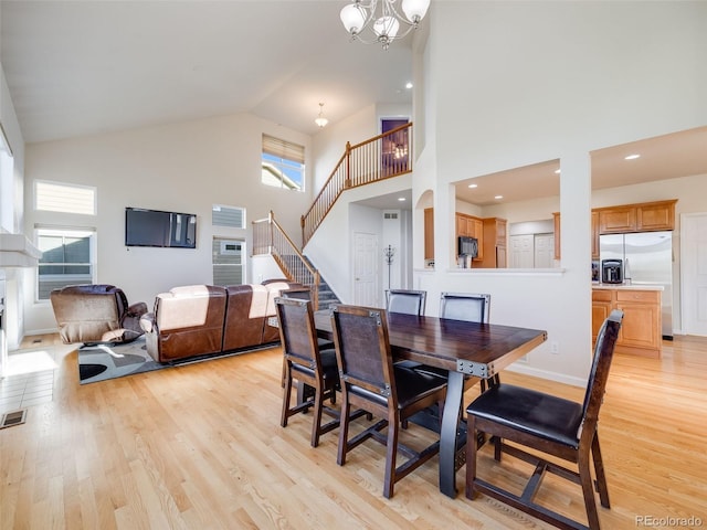 dining room with high vaulted ceiling, a chandelier, light wood finished floors, stairway, and a glass covered fireplace