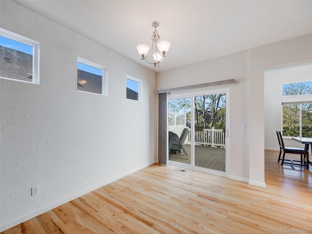 unfurnished dining area featuring a chandelier, light wood-type flooring, baseboards, and a textured wall