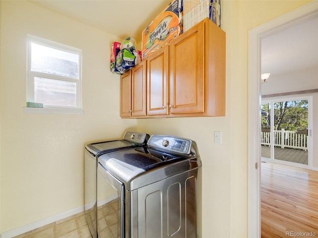 clothes washing area with washing machine and dryer, baseboards, and cabinet space
