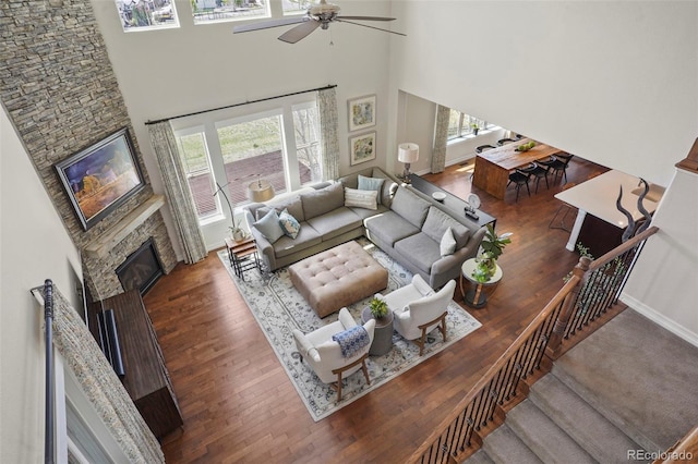 living room featuring a stone fireplace, ceiling fan, wood finished floors, and a wealth of natural light