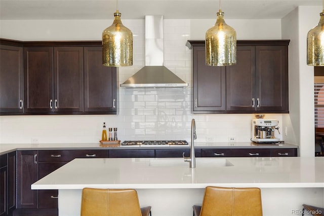kitchen featuring wall chimney range hood, decorative backsplash, dark brown cabinets, and decorative light fixtures