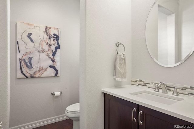bathroom with vanity, decorative backsplash, wood finished floors, toilet, and baseboards