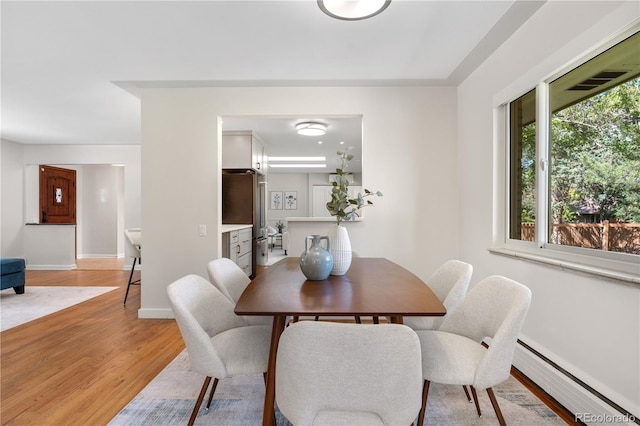 dining room with light wood-style flooring, a baseboard radiator, and baseboards
