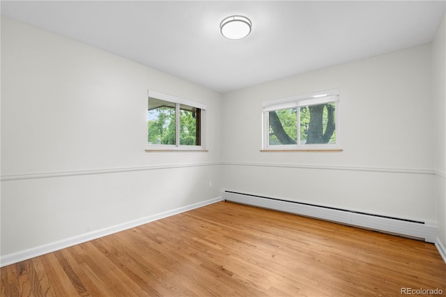 empty room featuring a baseboard heating unit, healthy amount of natural light, wood finished floors, and baseboards