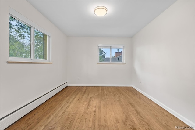 unfurnished room with a baseboard heating unit, plenty of natural light, light wood-style floors, and baseboards