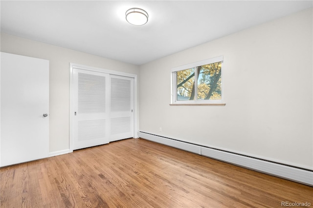 unfurnished bedroom featuring a baseboard radiator, wood finished floors, a closet, and baseboards