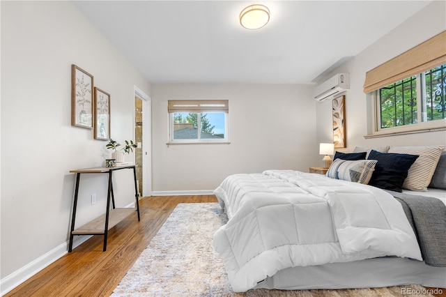 bedroom with a wall mounted AC, baseboards, and light wood-style floors