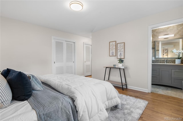 bedroom with light wood finished floors, ensuite bathroom, baseboards, and a sink