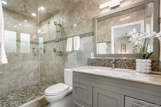 full bath with tile walls, a shower stall, toilet, vanity, and backsplash