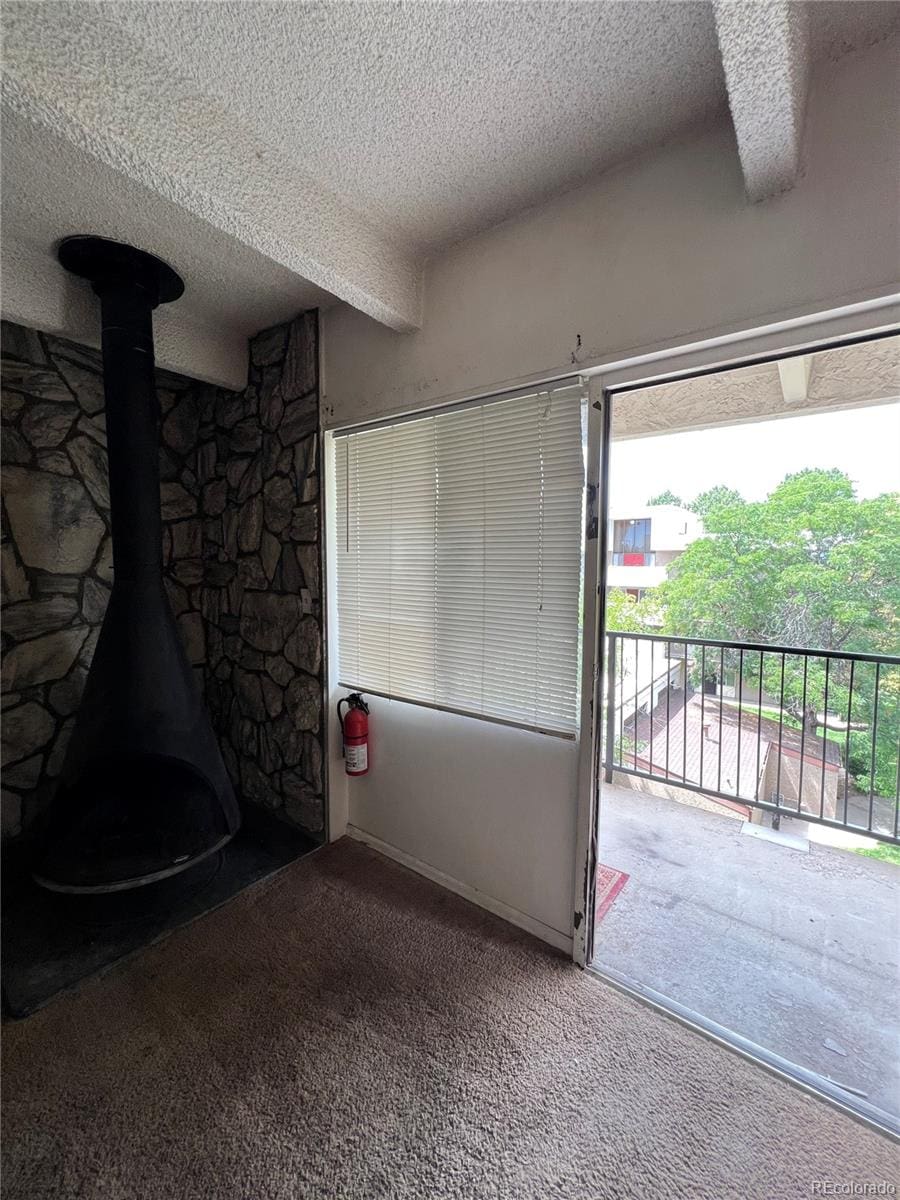 unfurnished living room with carpet floors, a textured ceiling, and a wood stove