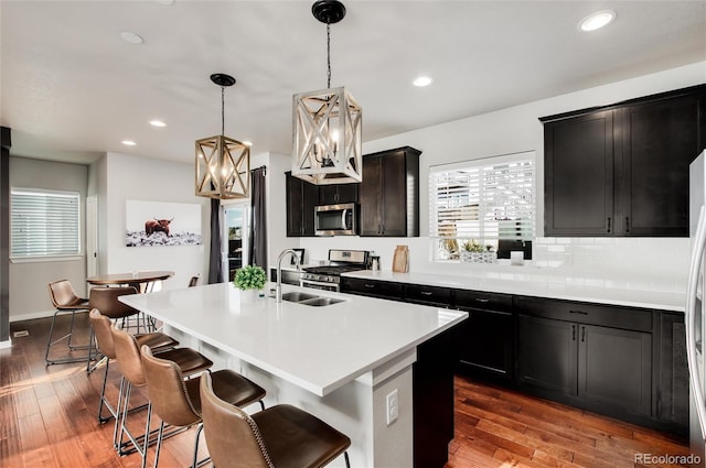 kitchen with pendant lighting, appliances with stainless steel finishes, sink, and a center island with sink