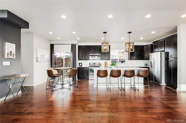 kitchen featuring hanging light fixtures, stainless steel appliances, a kitchen breakfast bar, and a center island with sink